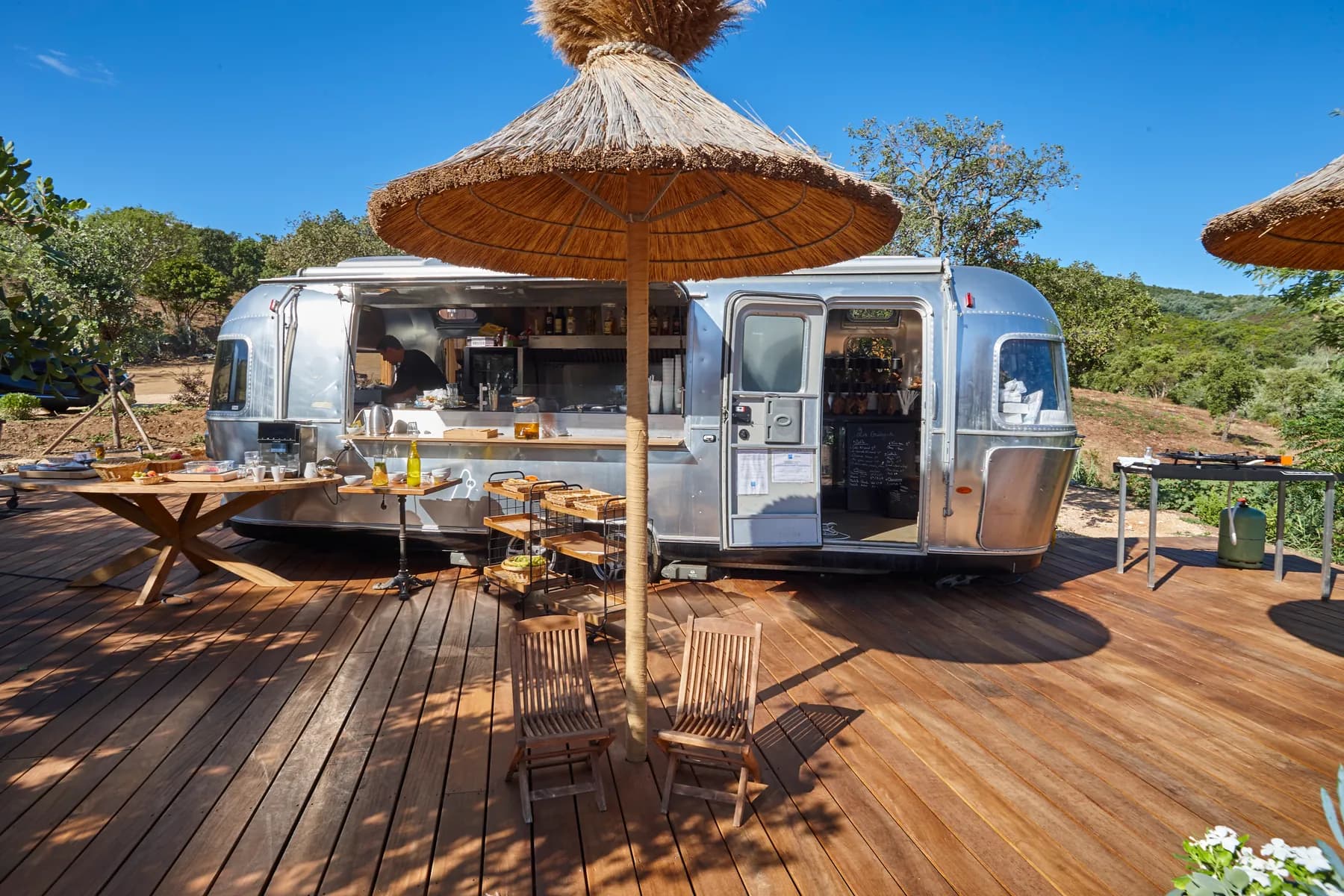 La caravane Airstream de face sous un grand parasol de paille